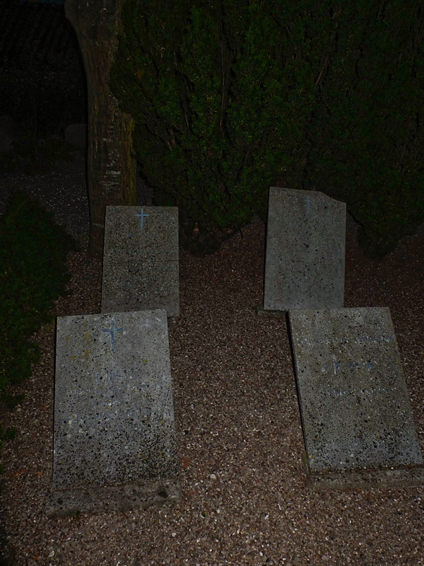 Fyra gravstenar på en mörk kyrkogård.